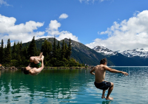 Zwei Männer springen in einen See vor Bergkulisse, Titelbild für Artikel "Neue Chefs in kaltem Wasser".